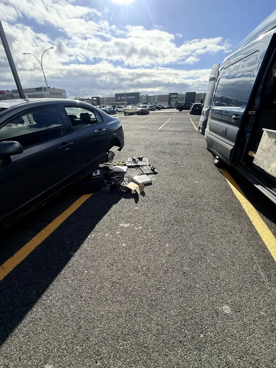 Honda Civic with the front wheel off in a shopping-centre parking lot, tools laid out, blue service van alongside