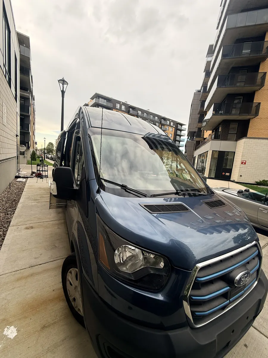 Blue Ford Transit service van parked on a residential street with tools set up on the sidewalk